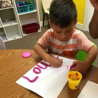 A Young Boy is Writing the Name Lou on a Piece of Paper