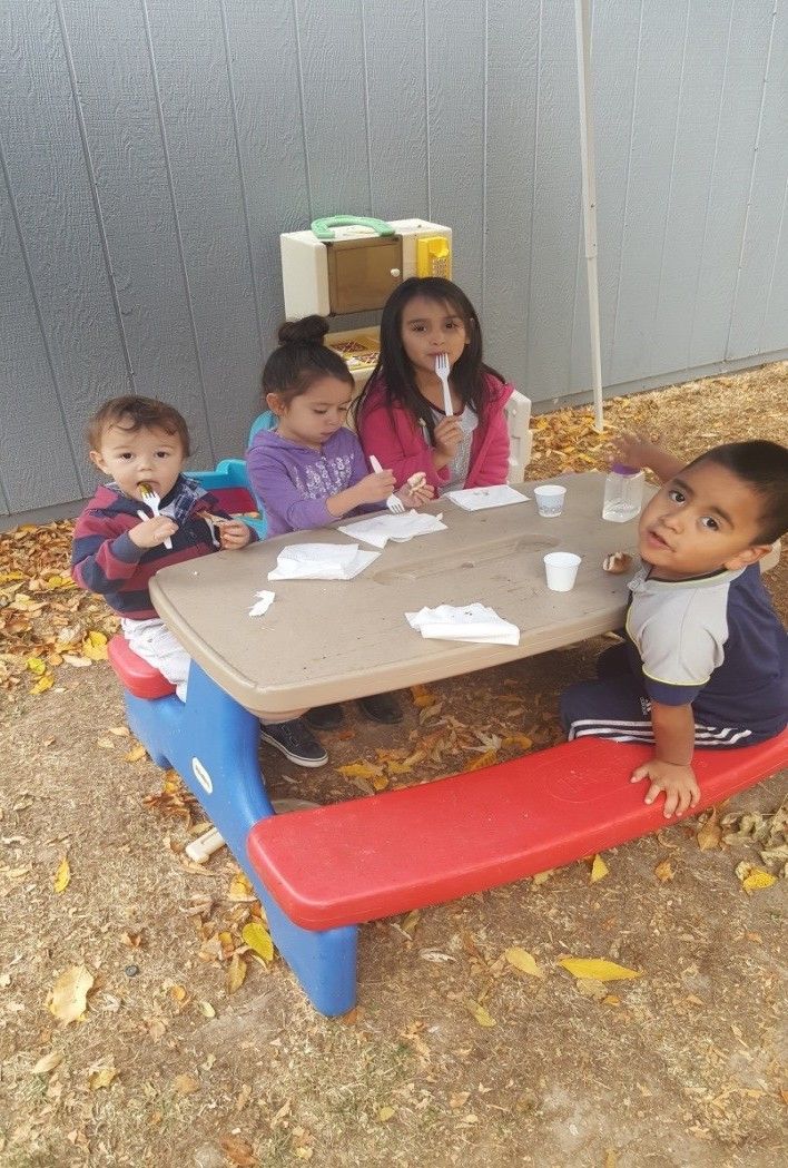 A group of children are sitting at a picnic table eating ice cream.