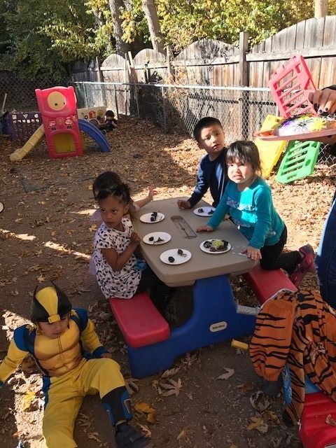 A boy in a wolverine costume sits at a table with other children