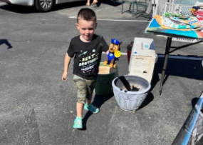 Boy in camo shorts and a black shirt walks toward the camera, a Paw Patrol figure sits on a flowerpot.