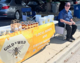 Man selling honey at an outdoor market, displaying jars and bags on a table with a