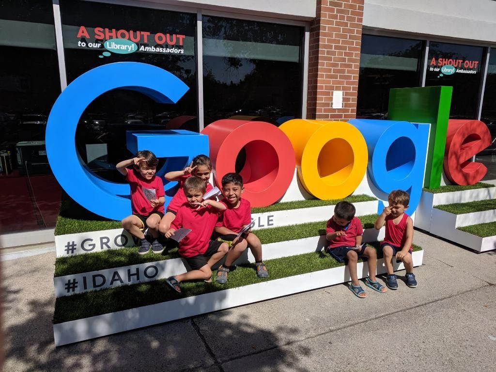 A group of children are sitting in front of a google sign.