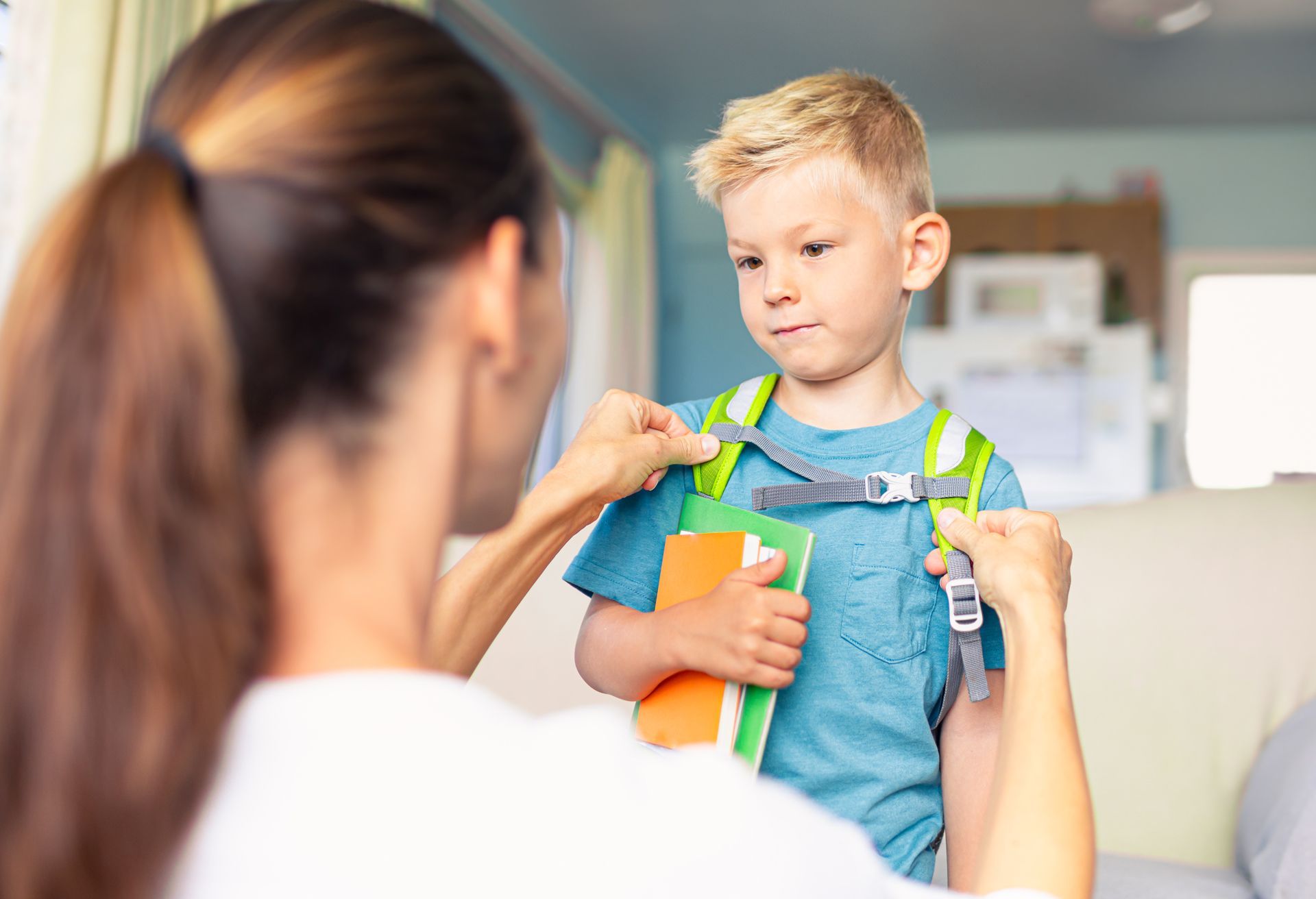 A Woman is Helping a Young Boy Put on His Backpack