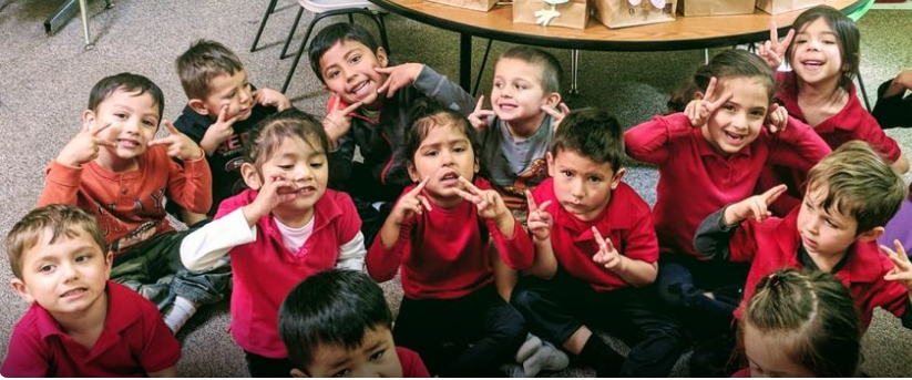 A Group of Children in Red Shirts Are Sitting on the Floor in a Classroom