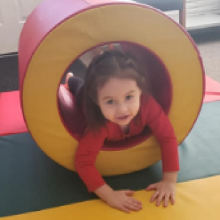 A Little Girl is Crawling Through a Red and Yellow Circle
