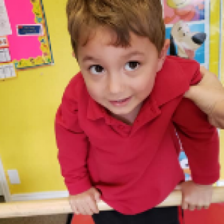 A Young Boy in a Red Shirt is Standing on a Bar