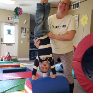 A Woman Holds a Child Upside Down in a Gym