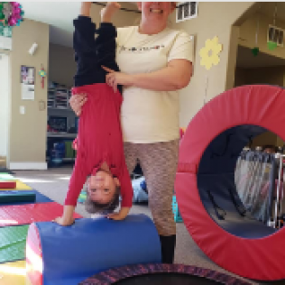 A Woman Holds a Child Upside Down in a Gym