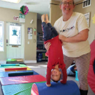 A Woman Holds a Child Upside Down in a Gym