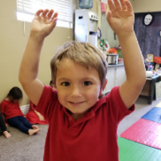 A Young Boy in a Red Shirt is Raising His Hands in the Air