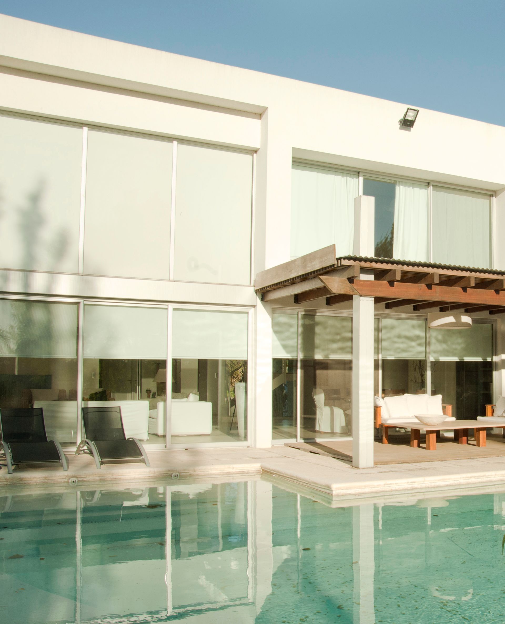 Casa blanca moderna con piscina; patio con asientos; escena exterior soleada.