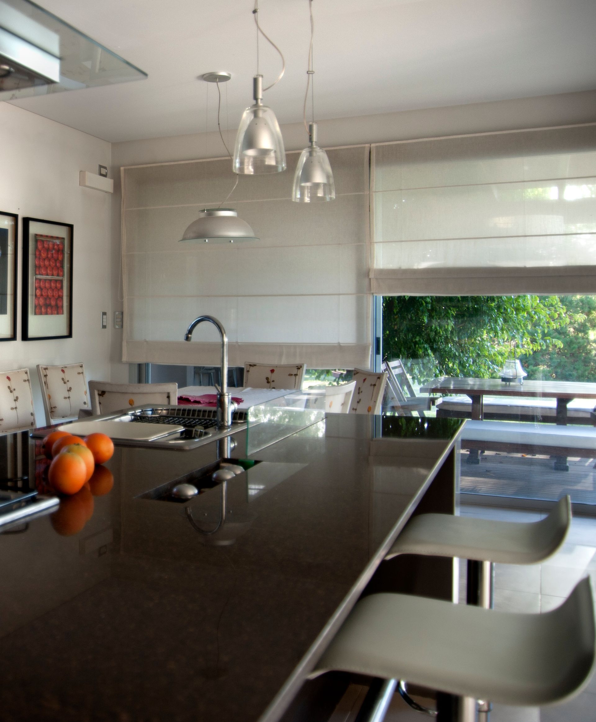 Cocina moderna con isla de granito oscuro, taburetes y vista a la vegetación.