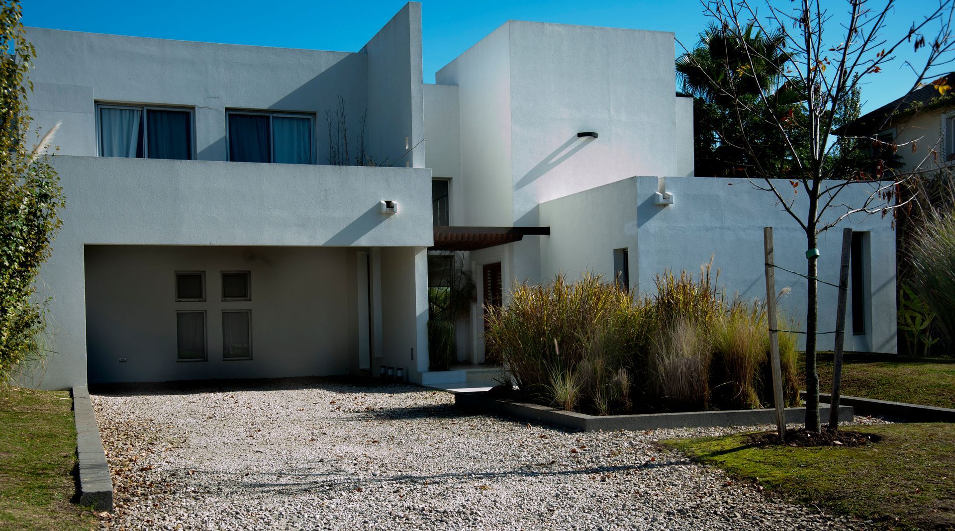 Casa blanca moderna con entrada de grava y pequeño patio delantero.