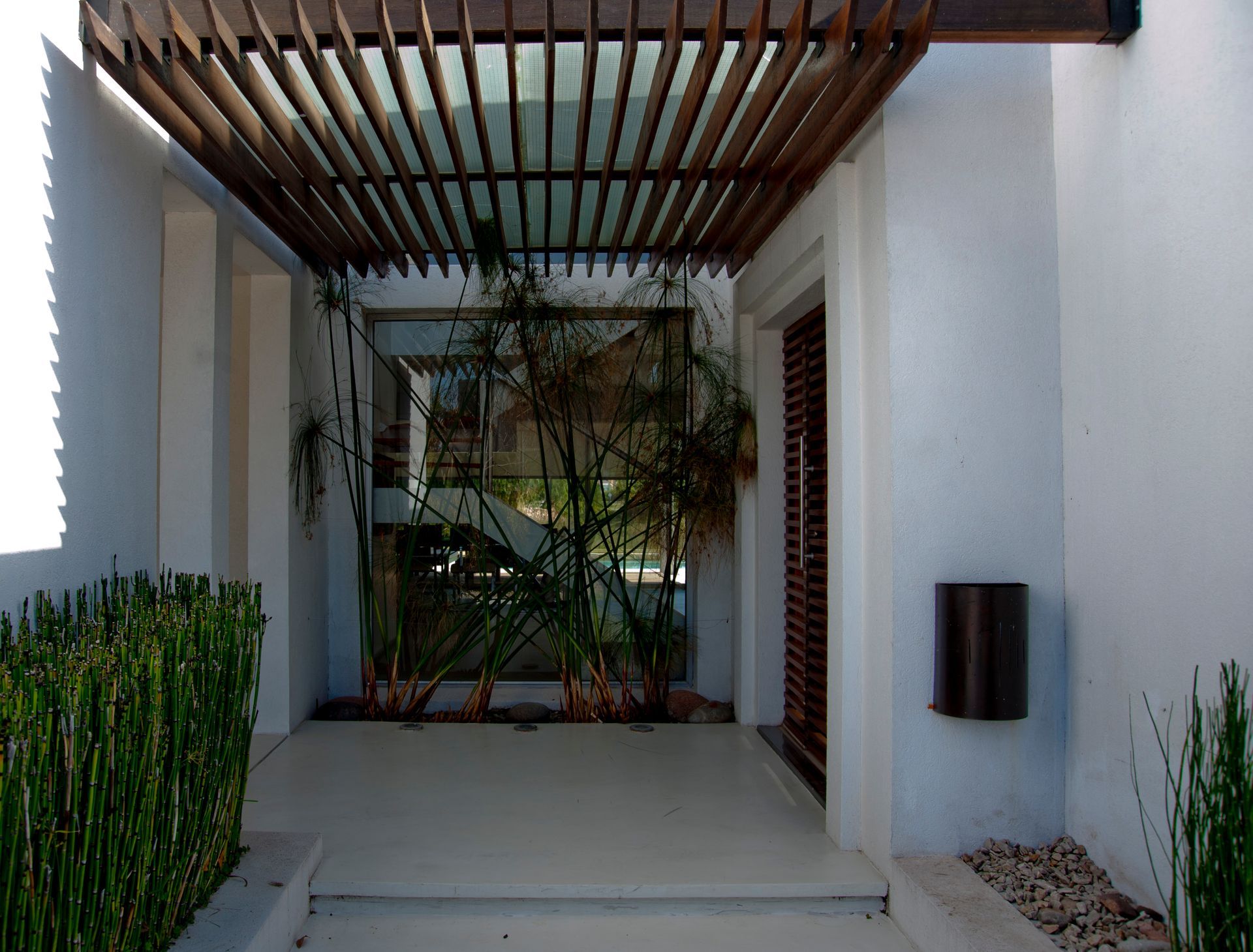Entrada con pérgola de madera, paredes blancas y plantas.