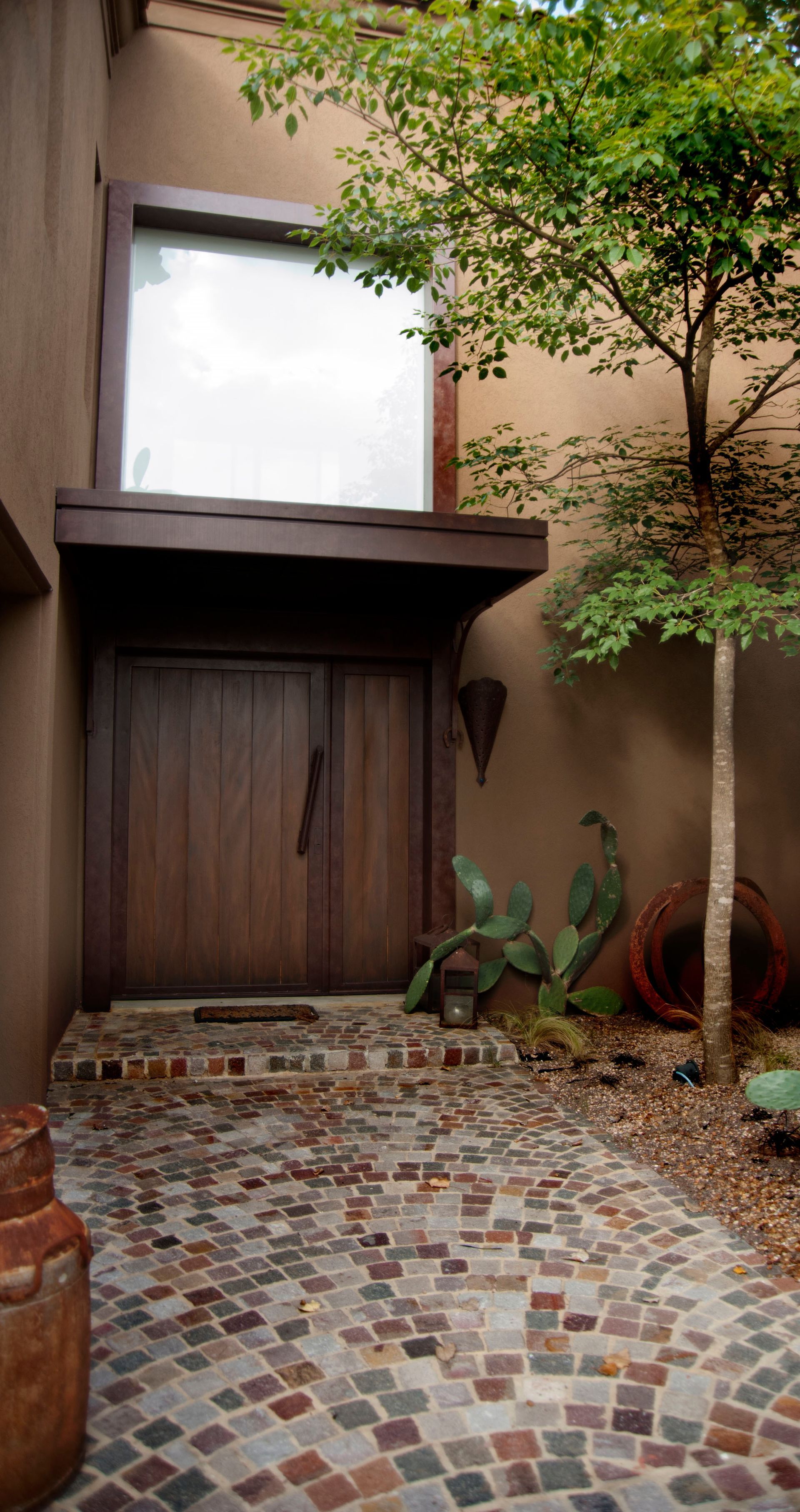 Puerta de madera con camino de piedra, enmarcada por paredes de estuco y un pequeño árbol.