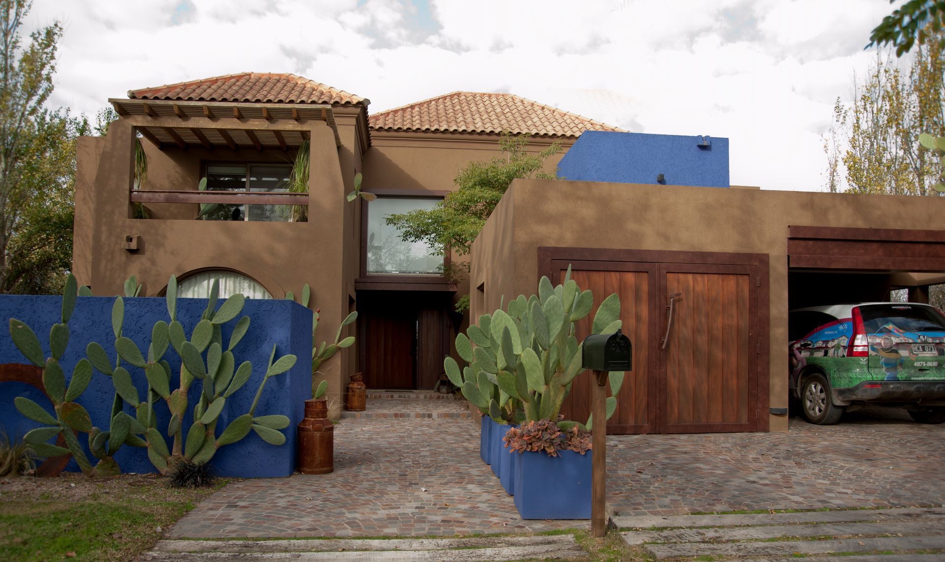 Casa de estuco color canela con detalles en azul, puerta de garaje de madera y un automóvil estacionado en el interior.