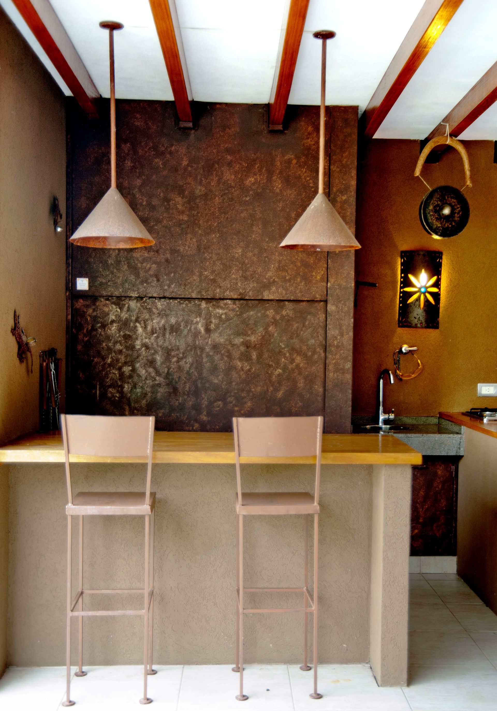 Barra con dos taburetes, lámparas colgantes, pared marrón y vigas de madera.
