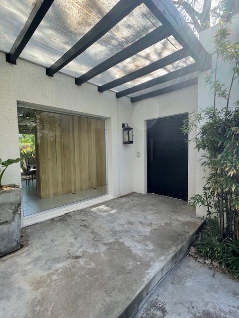 Entrada con rampa de hormigón, puerta negra, detalles de madera y techo sombreado.