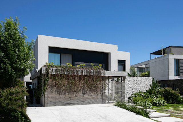 Casa moderna de dos plantas con paredes blancas y detalles en negro. Zona verde y entrada para coches. Cielo azul.