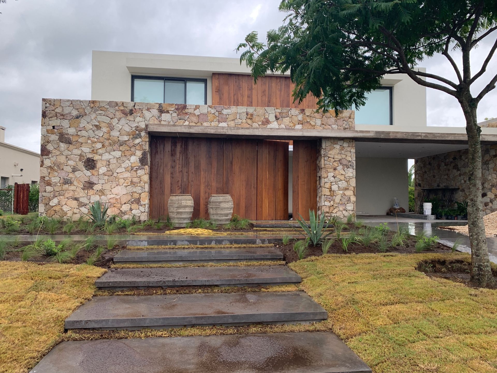 Casa moderna con fachada de piedra, puertas de madera y escalones que conducen a la entrada.