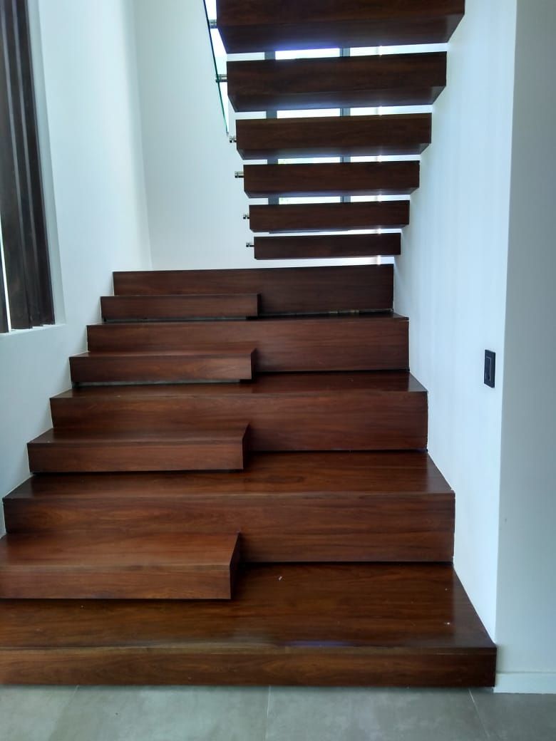 Escalera flotante de madera con peldaños oscuros sobre paredes blancas.