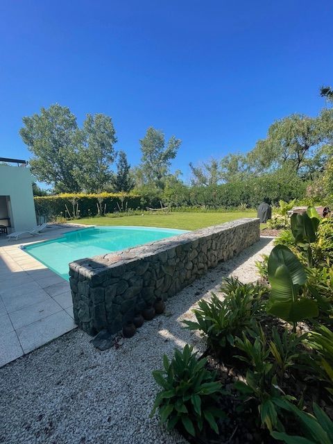 Escena junto a la piscina con pared de piedra, césped verde, cielo azul y follaje.