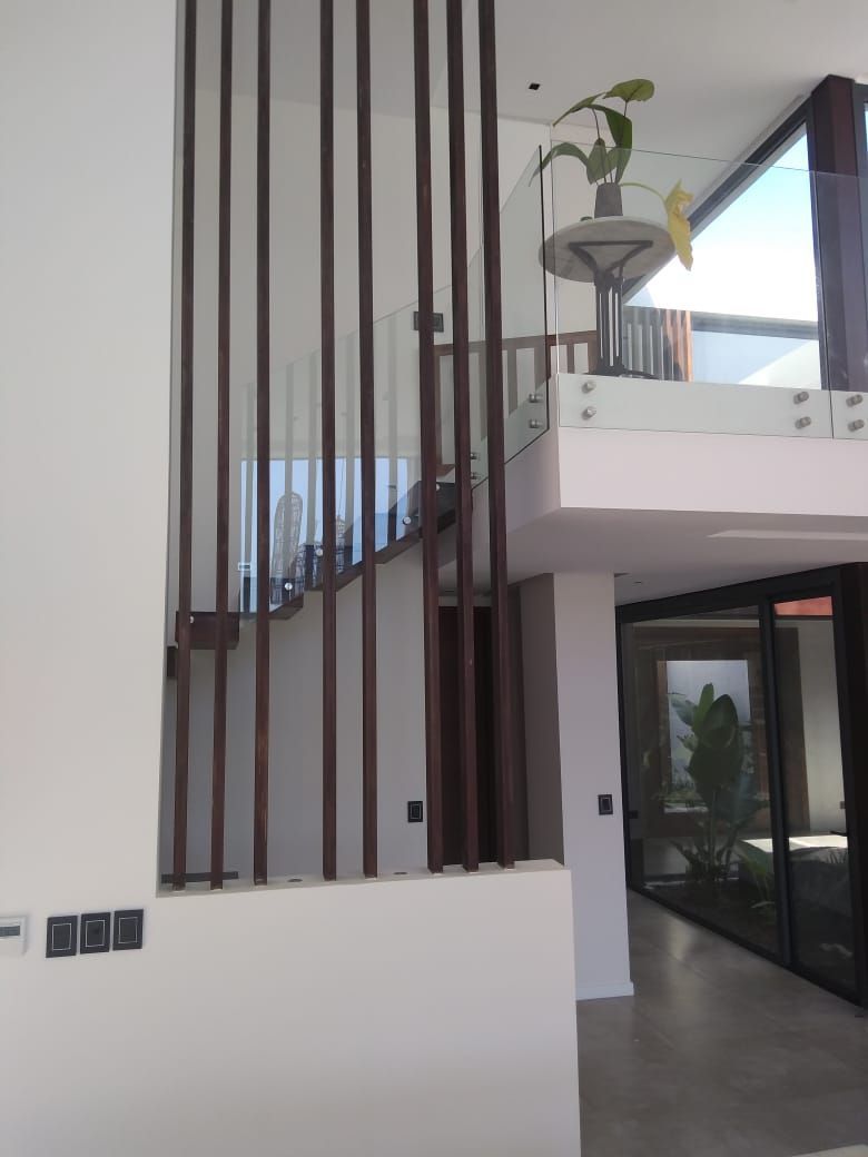 Interior de casa moderna con escalera, barandillas verticales marrones y barandilla de vidrio.