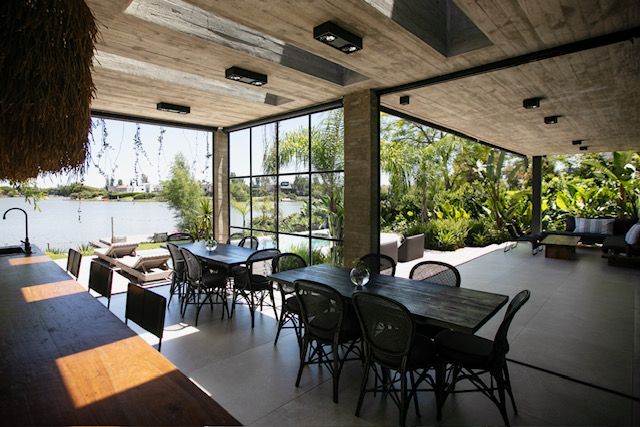 Comedor al aire libre con mesas, sillas, grandes ventanales y vista al mar.