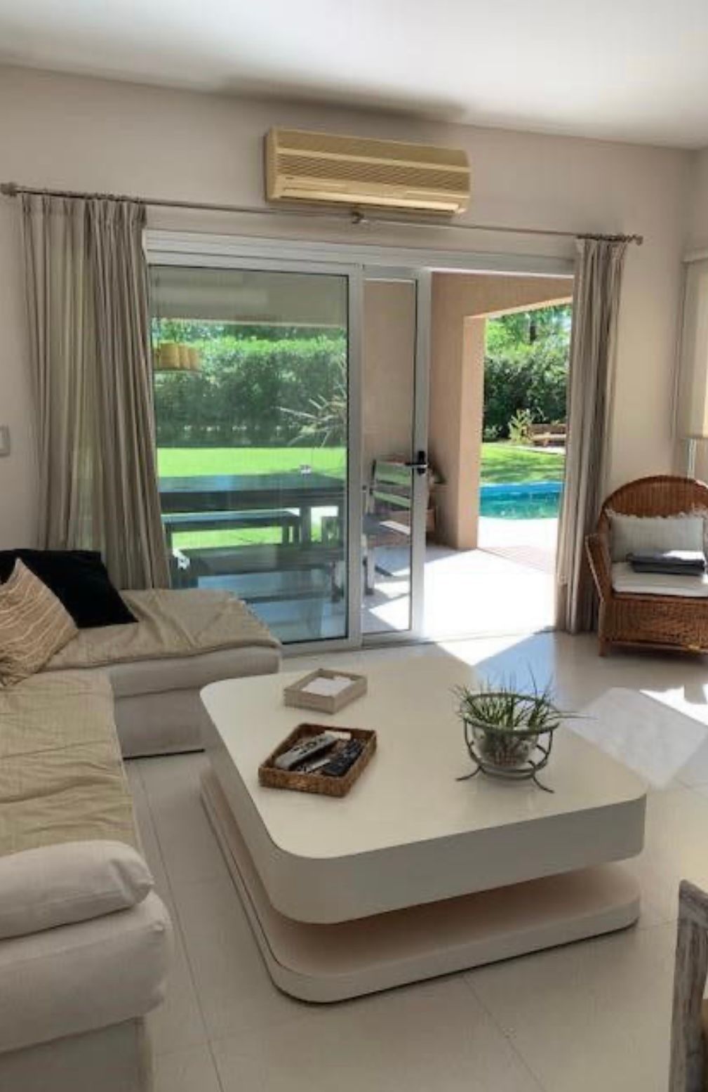 Sala de estar con muebles blancos, puertas de vidrio que se abren al patio y a la piscina.