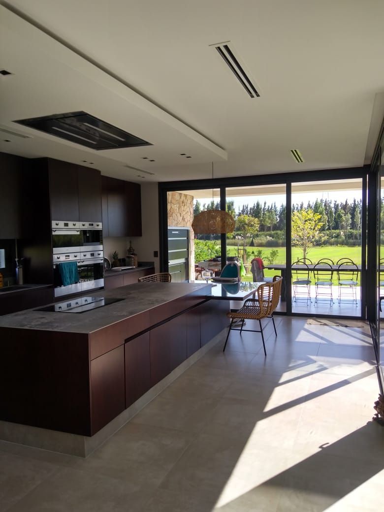 Cocina moderna con gabinetes oscuros, piso de color claro y grandes ventanales con vista a un paisaje verde.