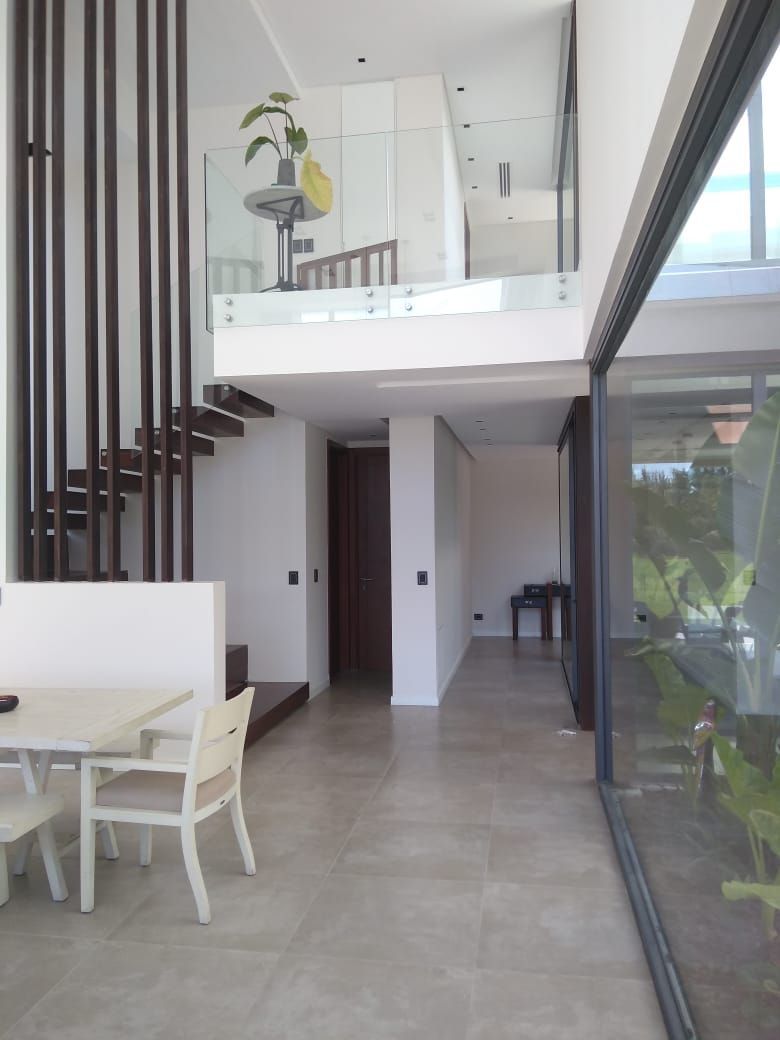 Interior de casa moderna: mesa de comedor, escalera, barandilla de vidrio y un pasillo con pared de vidrio.