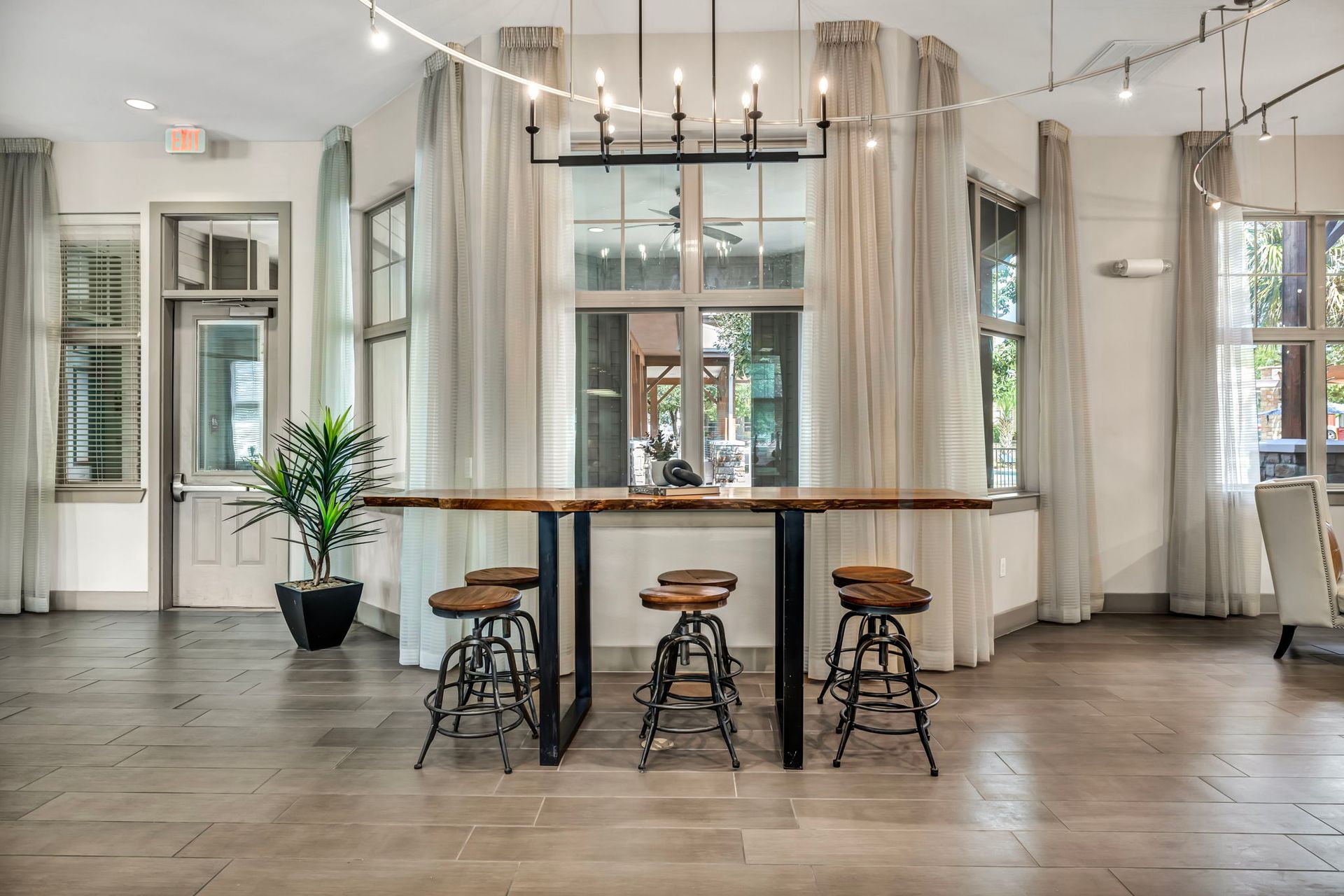 Room with bar, stools, large windows, and a chandelier; neutral colors.