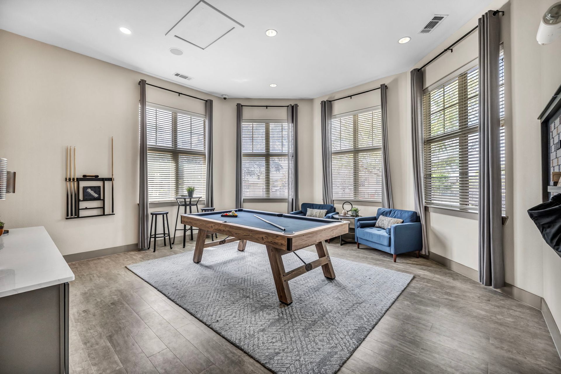 Pool table in a light-filled room with tall windows, blue armchair, and hardwood floors.