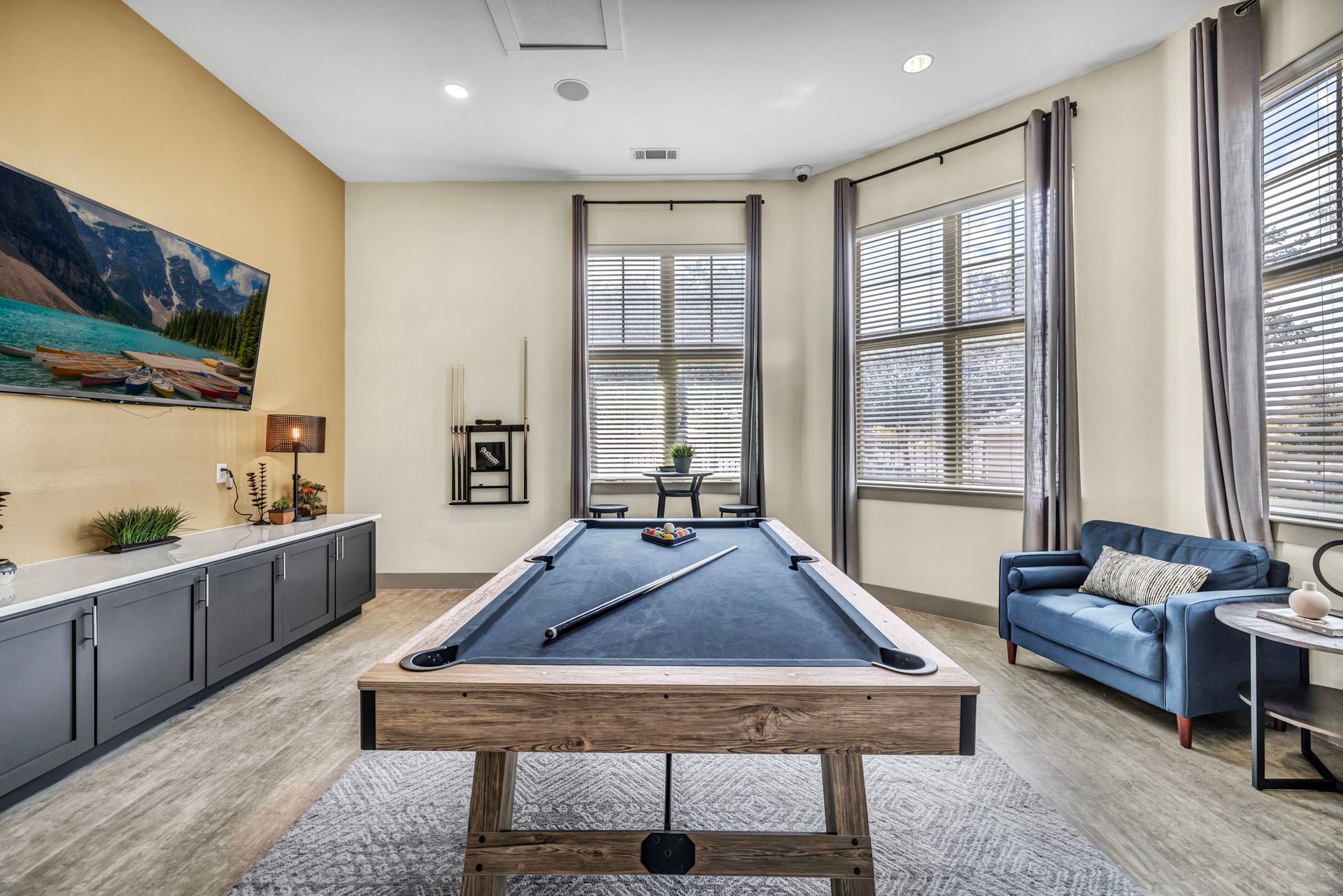 Pool table in a game room with blue accents, windows, and a sofa.