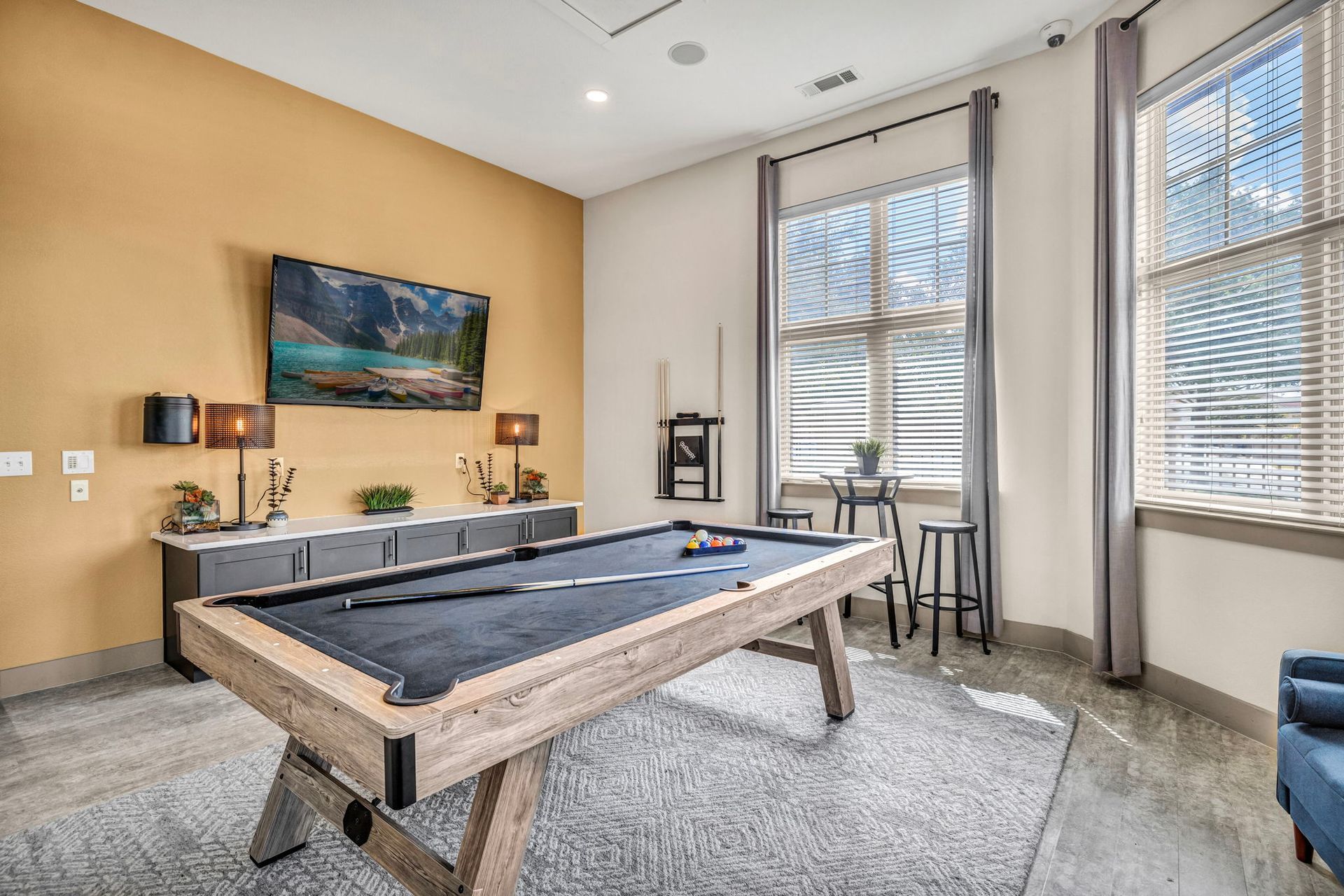 Pool table in a game room with a TV, window, and bar stools.