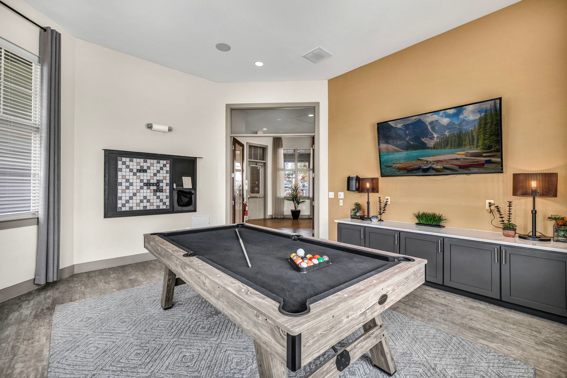 Pool table in a recreational room with gray cabinets, dartboard, and large TV.