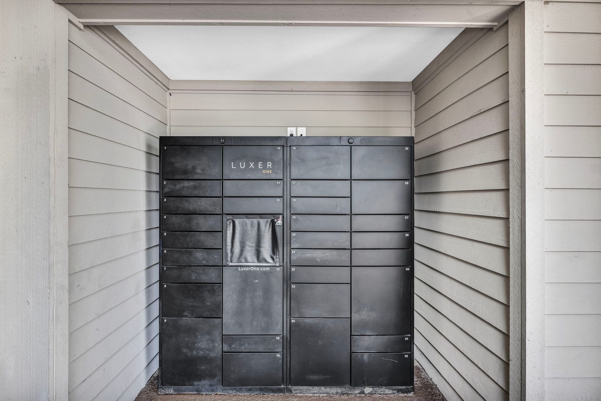 Black package lockers set into a recess in a building with light siding.