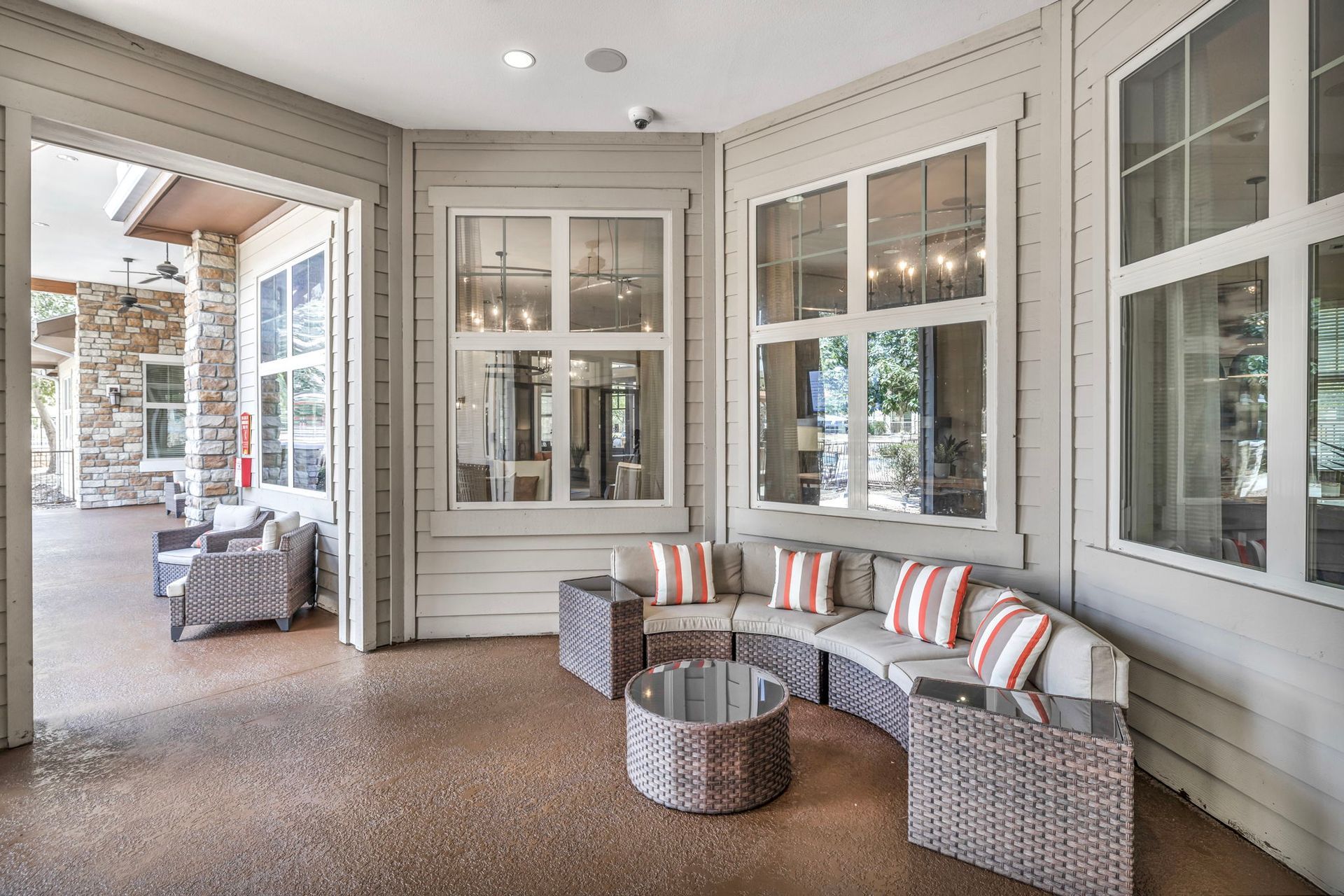 Outdoor seating area with curved wicker sofa, glass coffee table, and large windows.