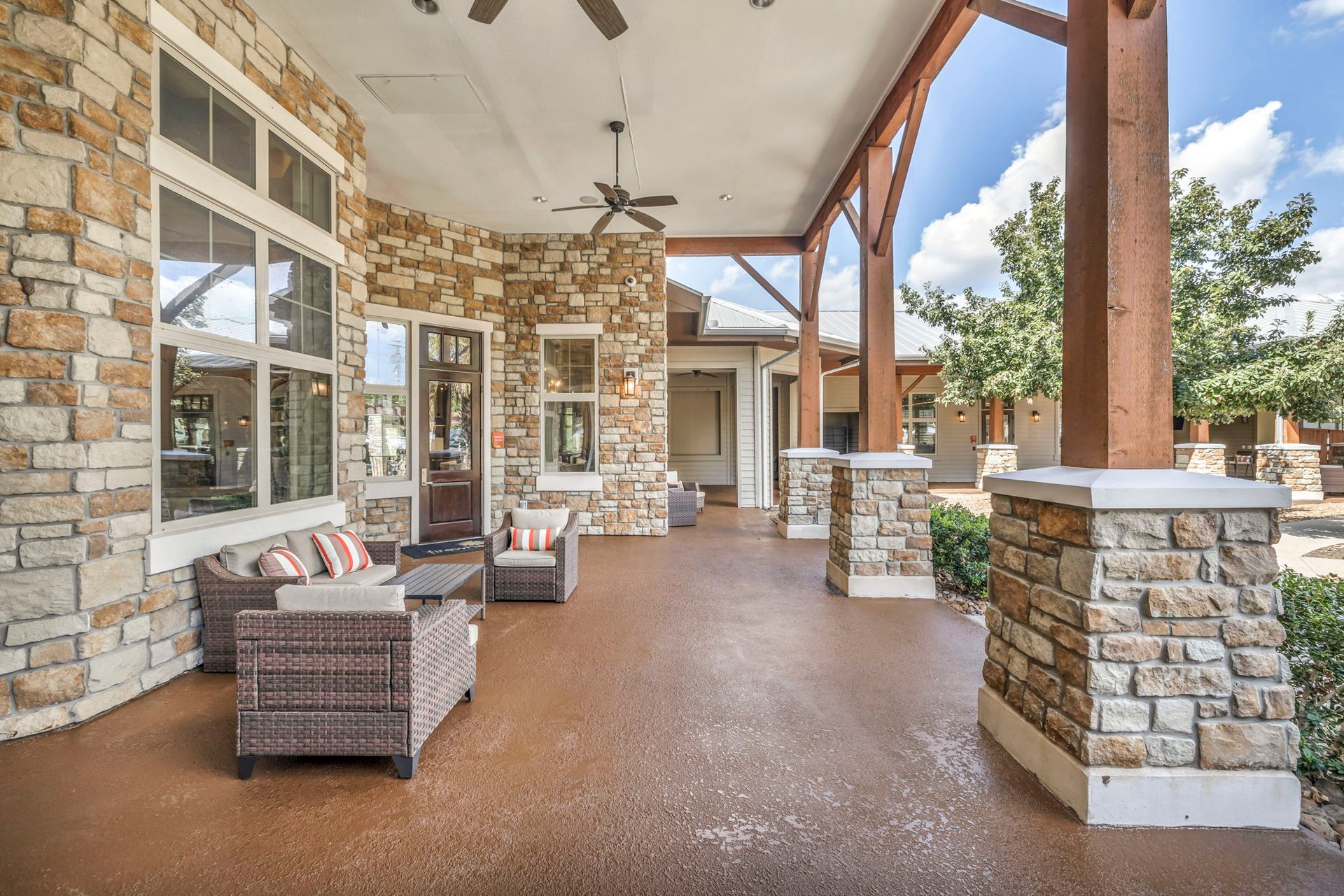 Covered patio with stone columns and walls, seating area, and trees in the background.