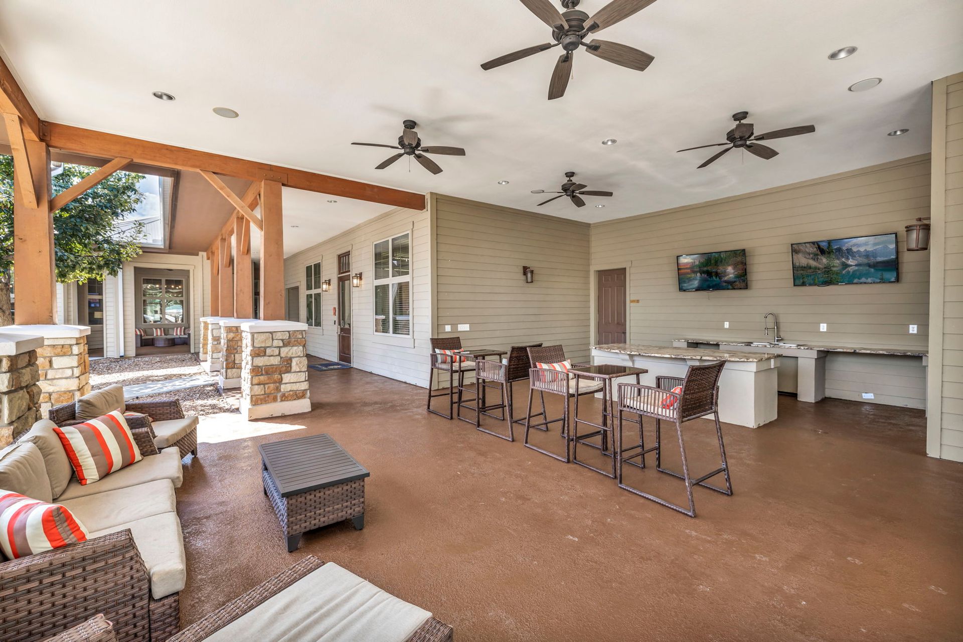 Covered patio with seating, bar area, and mounted TVs. Brown, beige, and neutral tones.