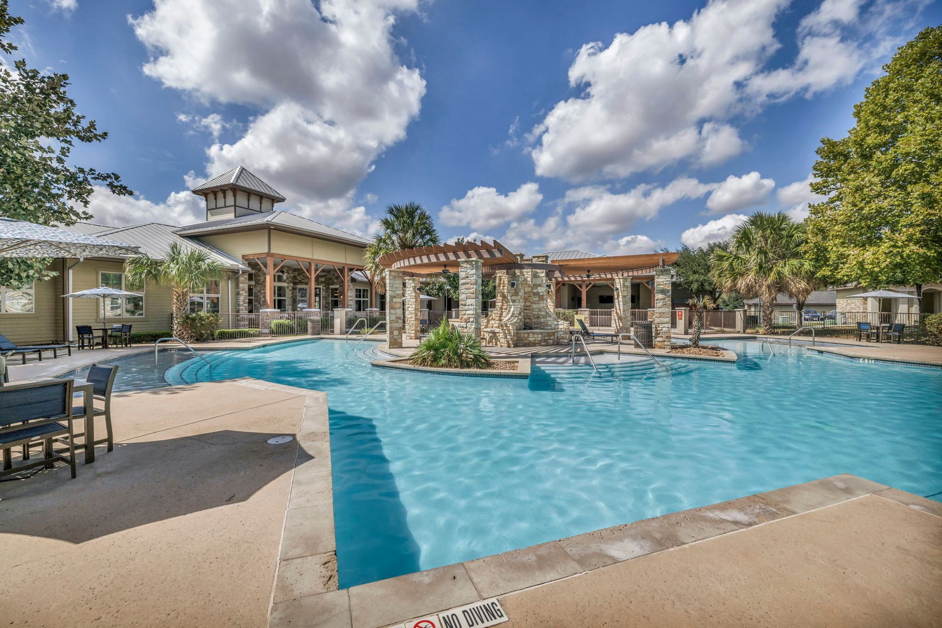 Swimming pool with a stone gazebo under a blue sky with puffy white clouds.