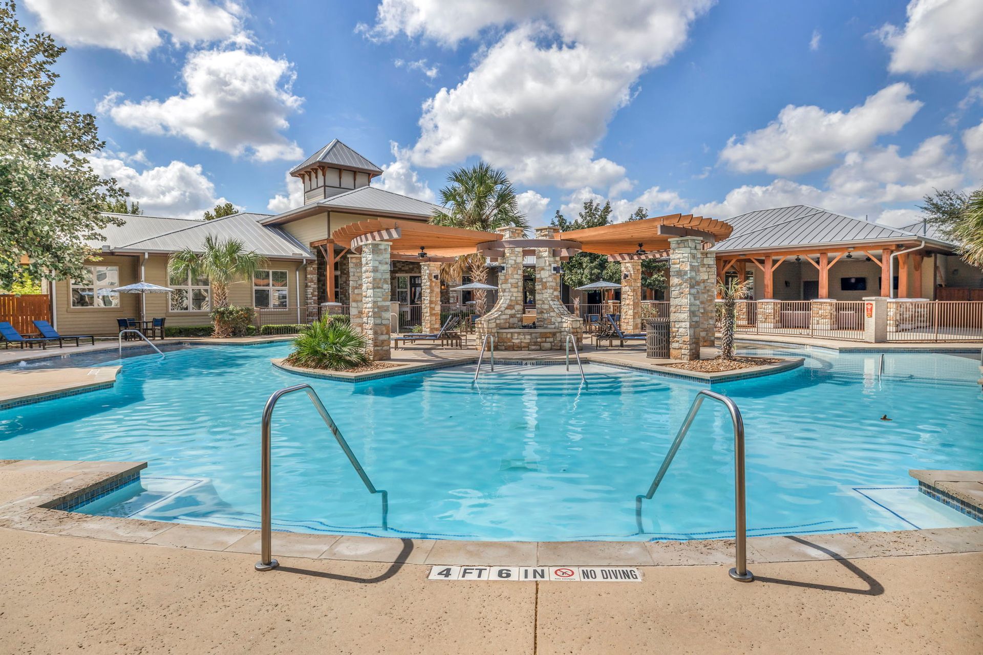 Swimming pool with a gazebo and waterfall feature, blue water, sunny day.