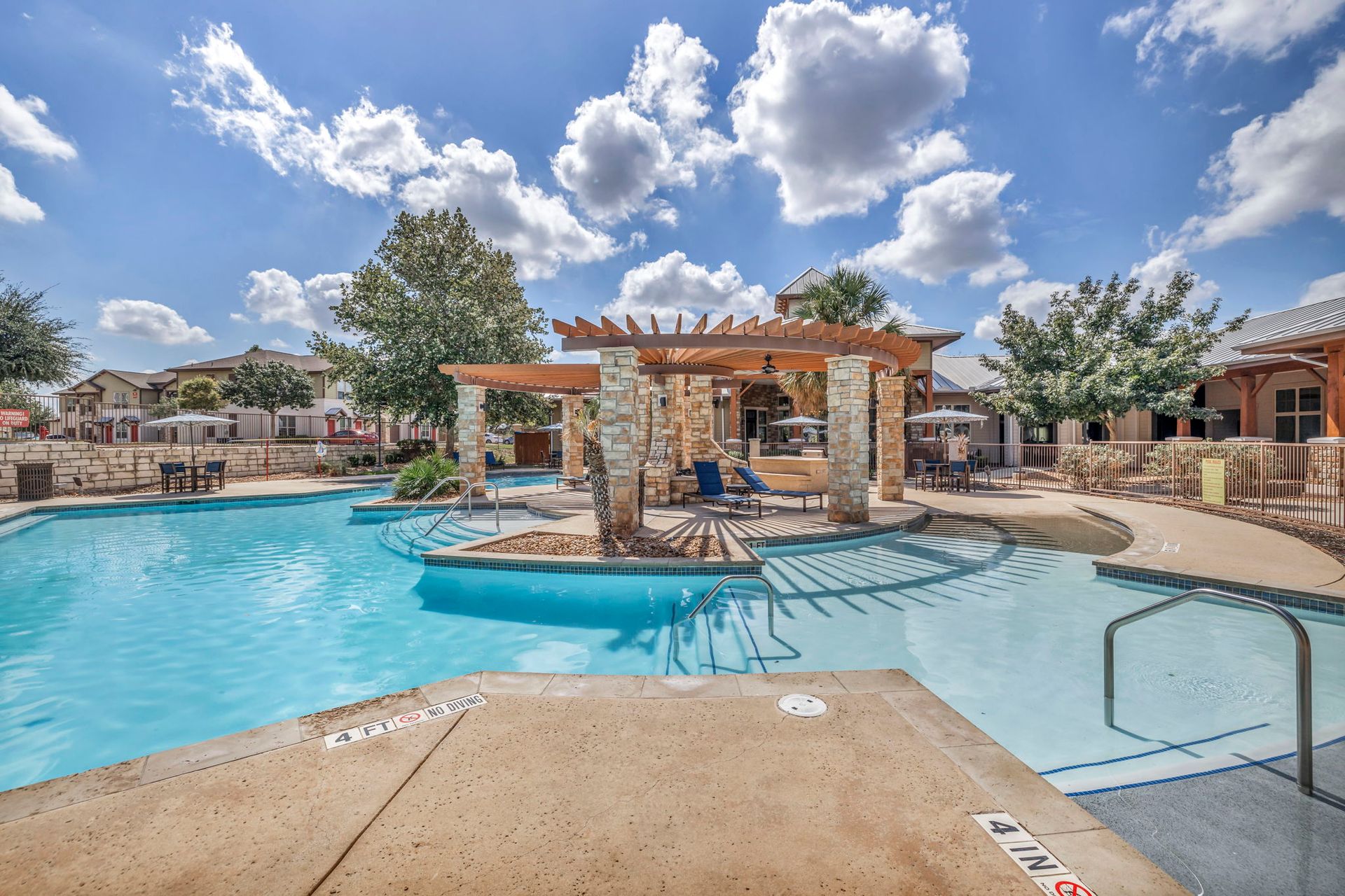 Pool with a wooden pergola and lounge chairs on a sunny day.
