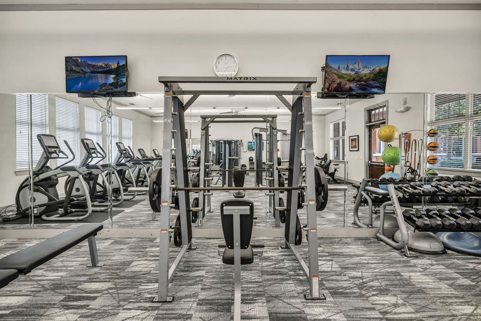Gym interior with exercise equipment, mirrors, and two televisions.