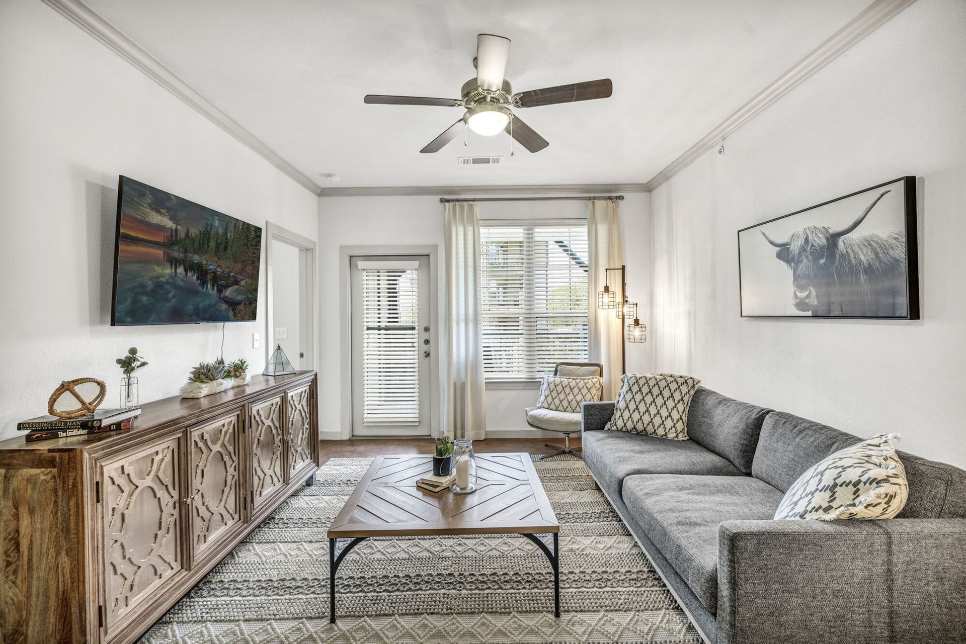 Living room with gray couch, wooden cabinet, and window with a ceiling fan above.