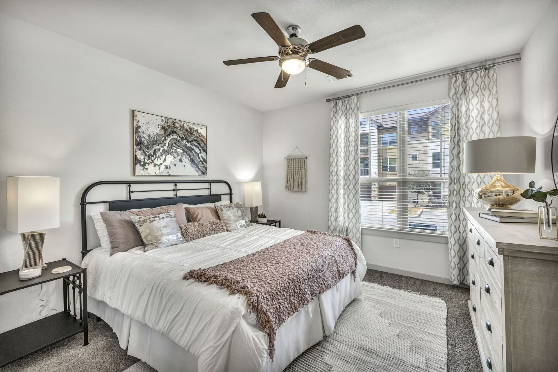 Cozy bedroom with a bed, nightstands, dresser, window, and ceiling fan. Neutral colors and soft textures.