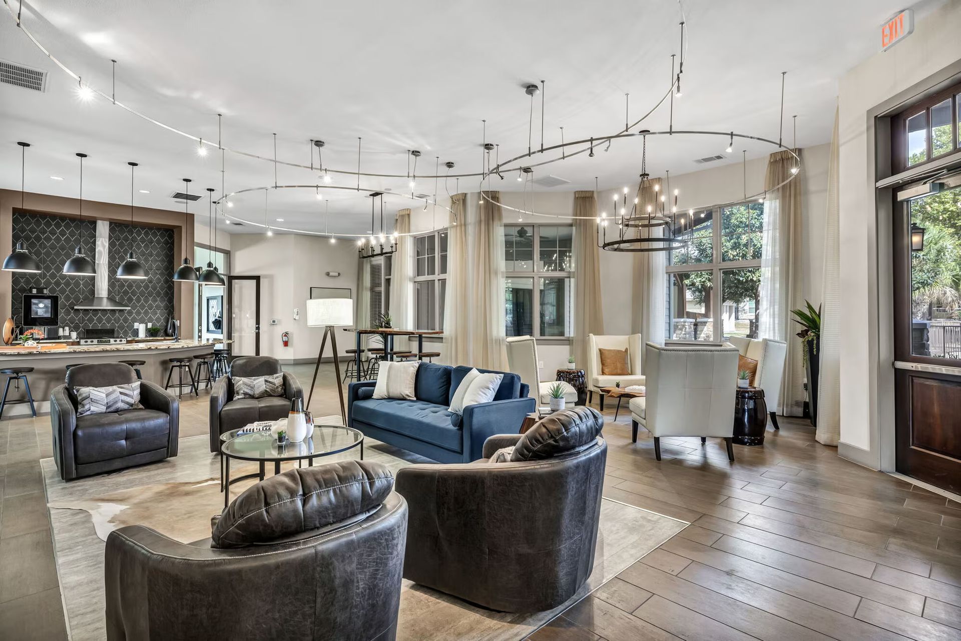 Open-plan lounge area with seating, kitchen, and large windows; neutral tones with pops of blue.