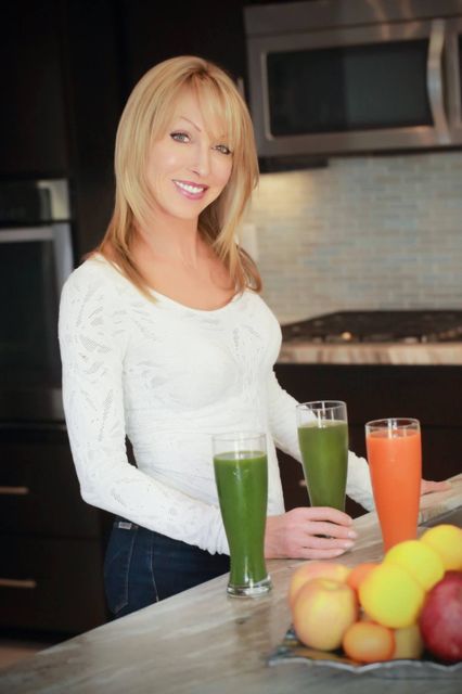 A woman is standing in a kitchen holding two glasses of juice