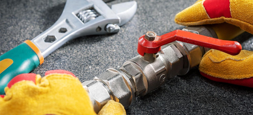 Adjustable wrench, plumbing valve, and work gloves on a textured surface.