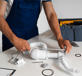 Plumber measuring white sink pipes, tools in background.